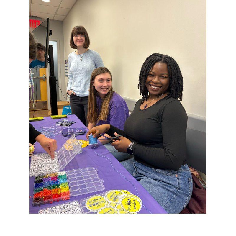 Three students sitting at a table and posing for a photo during a craft activity.